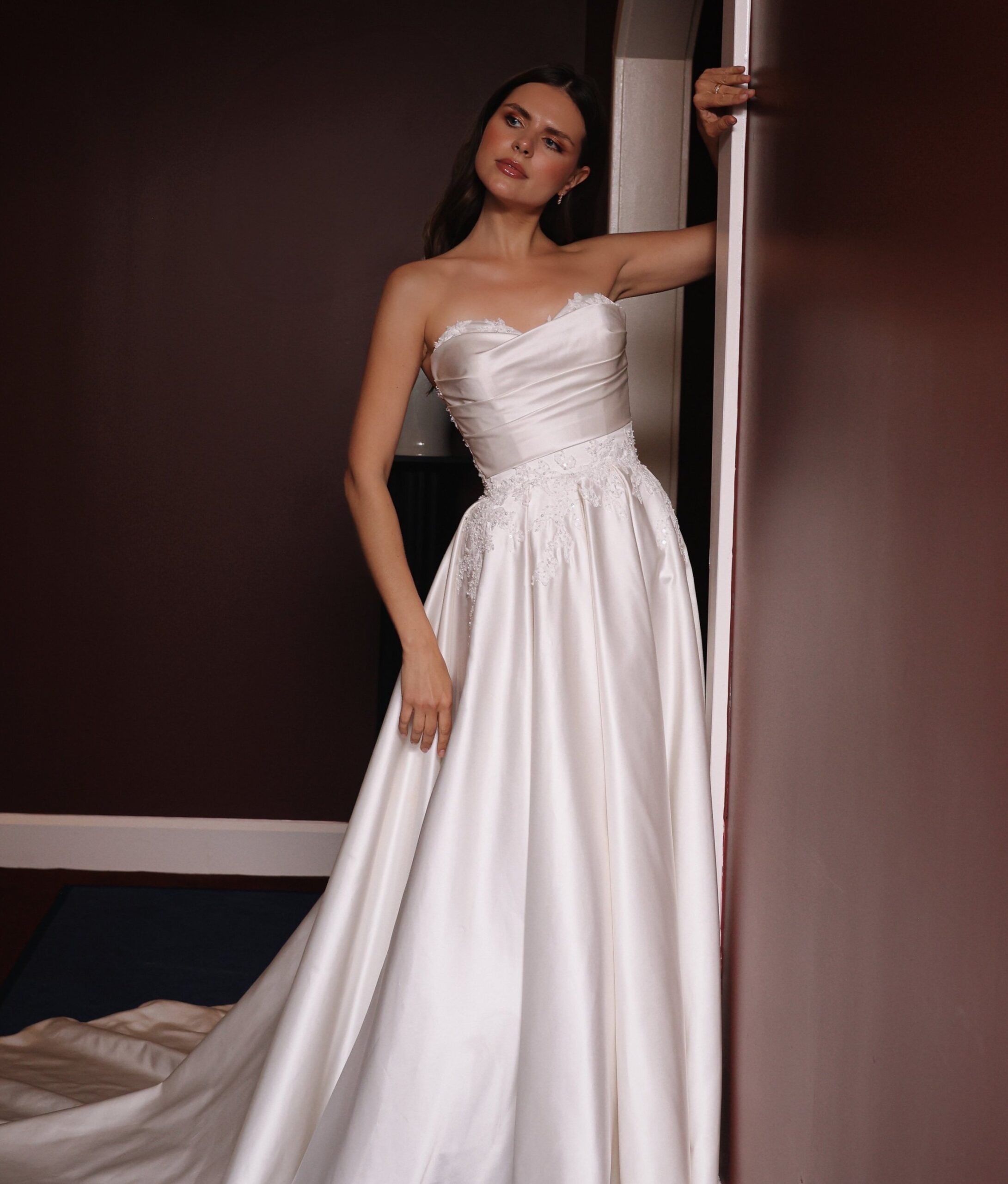 A woman in a white wedding dress standing near a doorway in a dimly lit room.