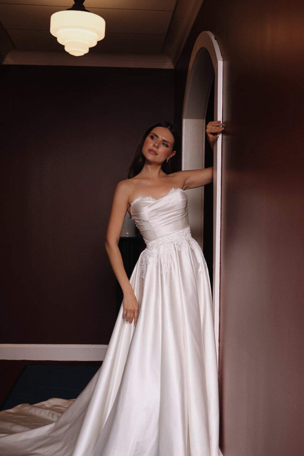 A woman in a white wedding dress standing near a doorway in a dimly lit room.