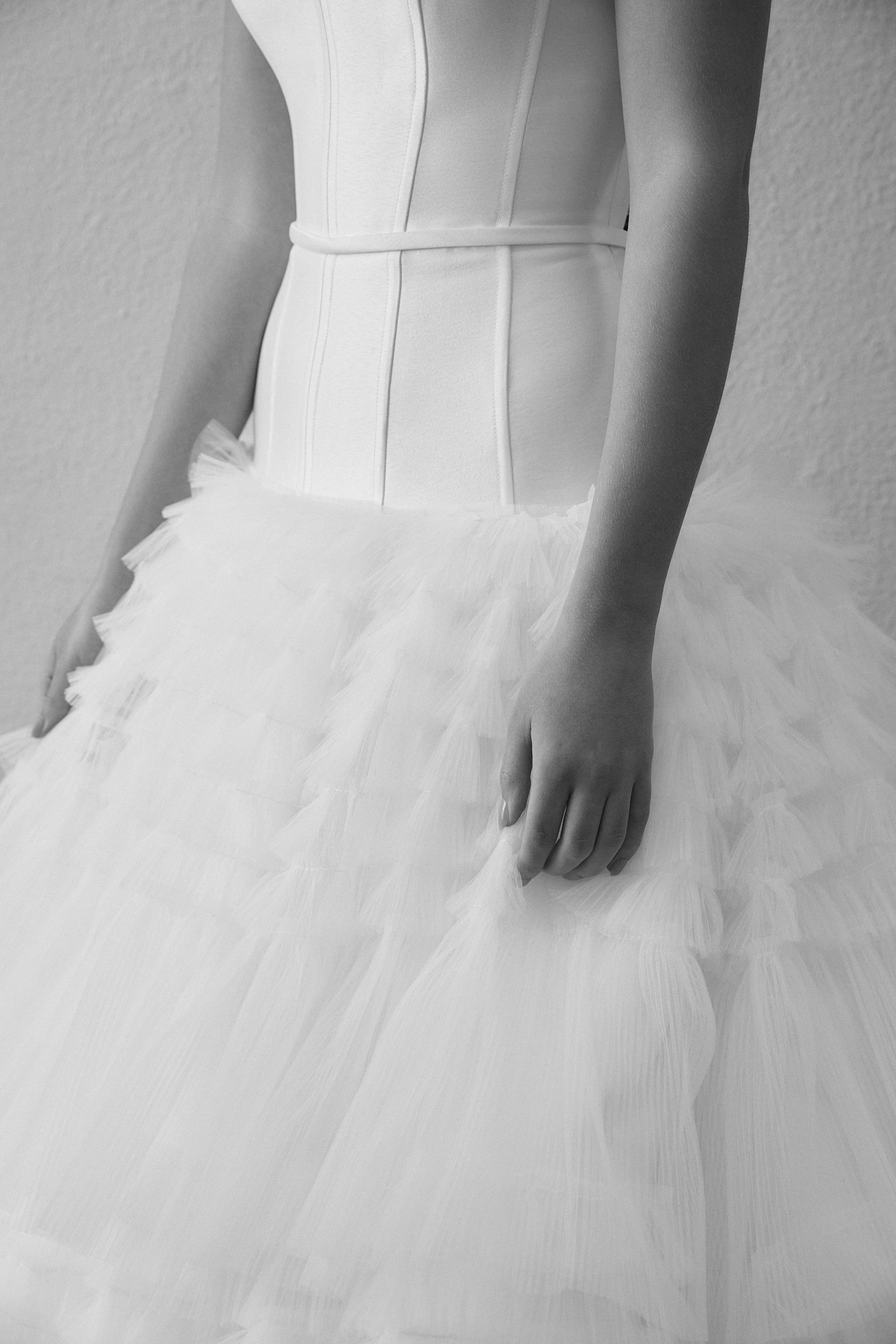 Close-up of a person wearing a white corset and a tulle skirt, with their hands resting on the skirt.